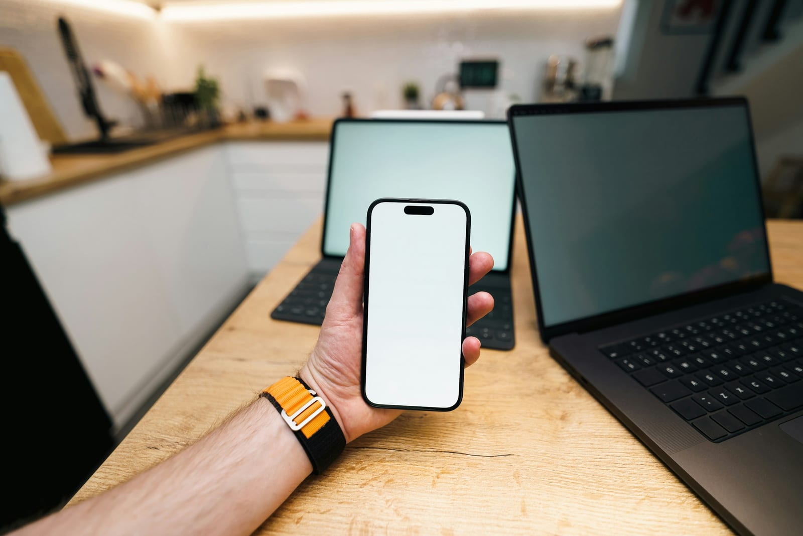 Ruka drži mobitel ispred laptopa kao ilustracija poslovnog rada s digitalnim i AI alatima.
