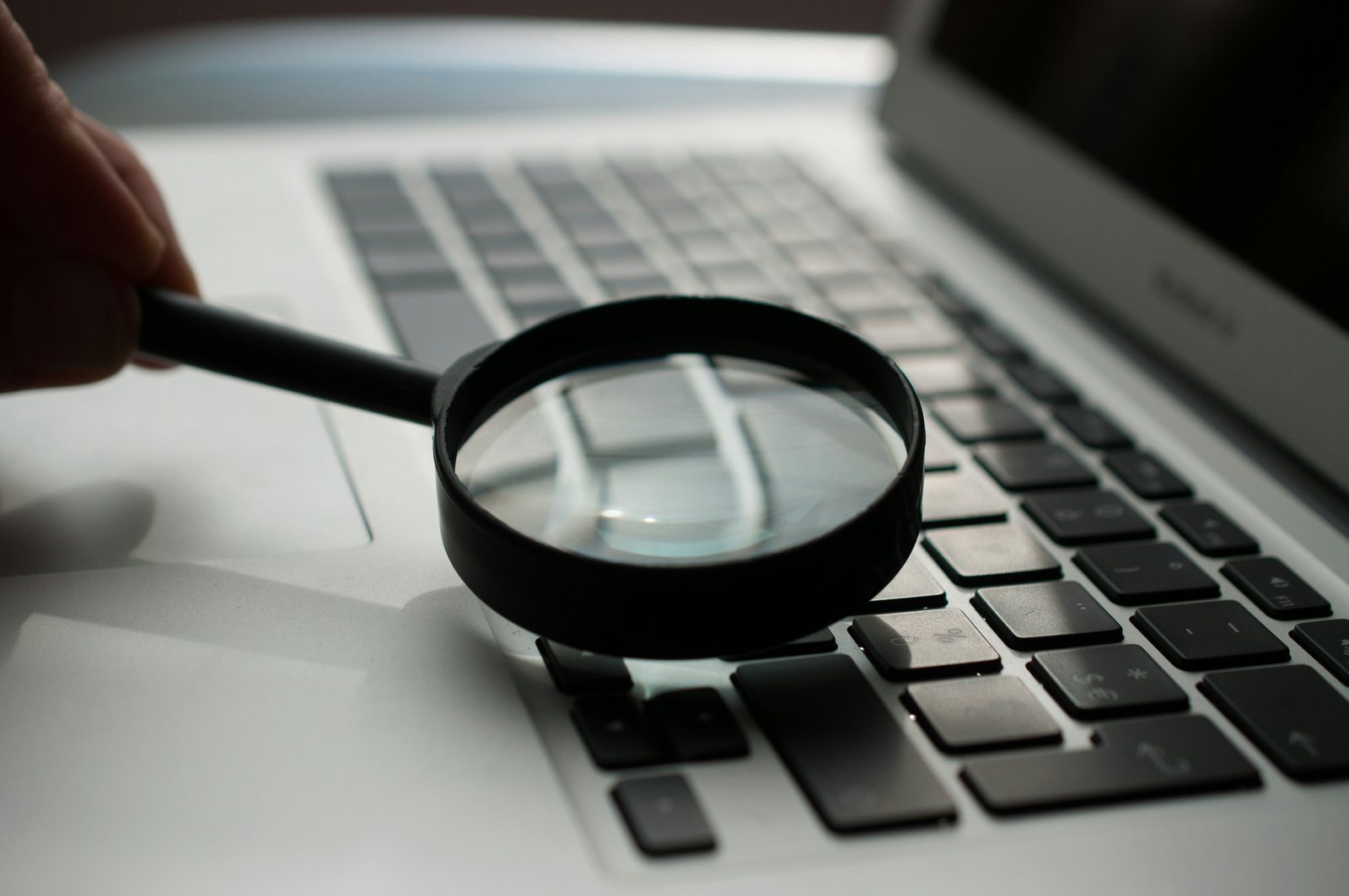 Povećalo iznad tipkovnice laptopa kao metafora za provjeru izvora i točnosti informacija.